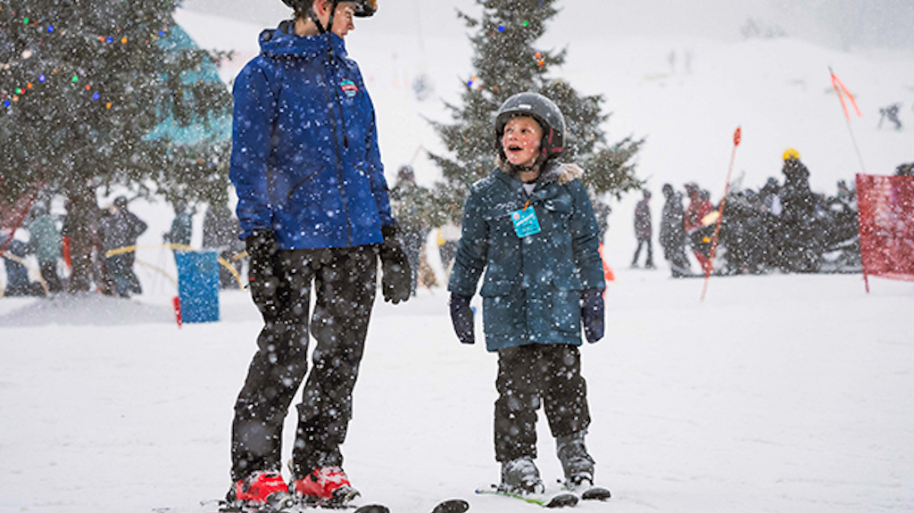 A young boy looks up at his ski instructor with a look of joy on a snowy day.